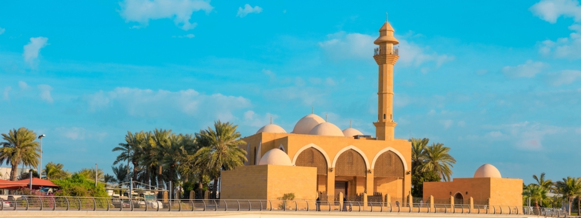 A mosque with a tall minaret, surrounded by palm trees under a clear blue sky.
