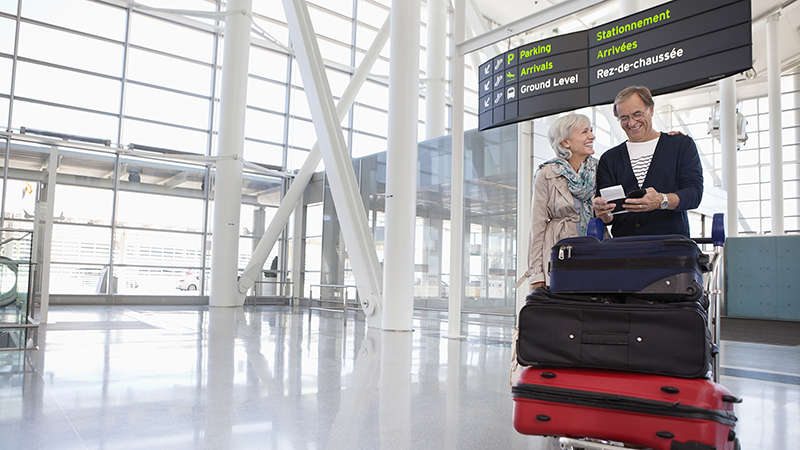 Əllərində yük olan yaşlı cütlük aeroportda Smiling couple with full luggage trolley in airport.