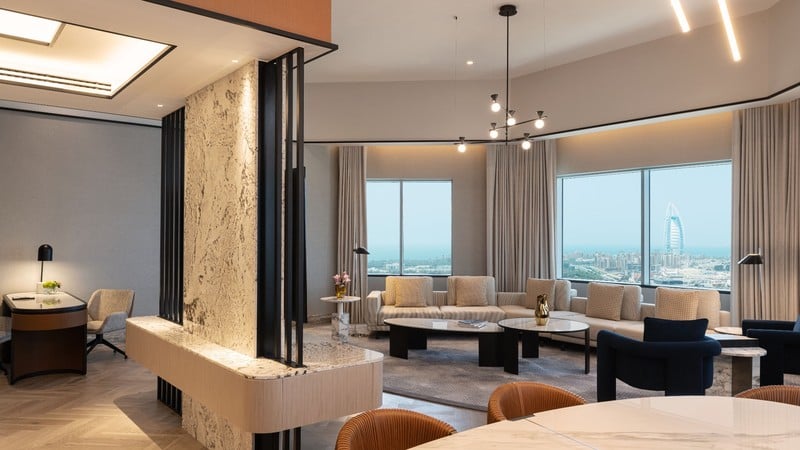 Spacious modern living room with large windows, contemporary furniture, decorative lighting, and a view of a cityscape with a prominent tower in the background.