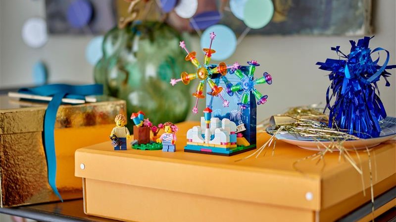 A toy Ferris wheel and two figures are displayed on an orange box alongside a gold box and blue decorative items.