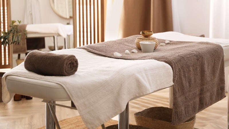 Massage table with rolled towel, brown blanket, and decorative stones in a serene spa setting.