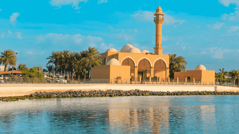 A mosque with a tall minaret, surrounded by palm trees under a clear blue sky.